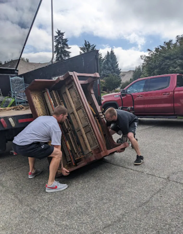 Two of the crew lifting an upright piano into the truck